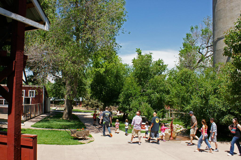 Families strolling through a sunny day at Lee Martinez Park, with children exploring and adults enjoying the green surroundings and rustic farm buildings.