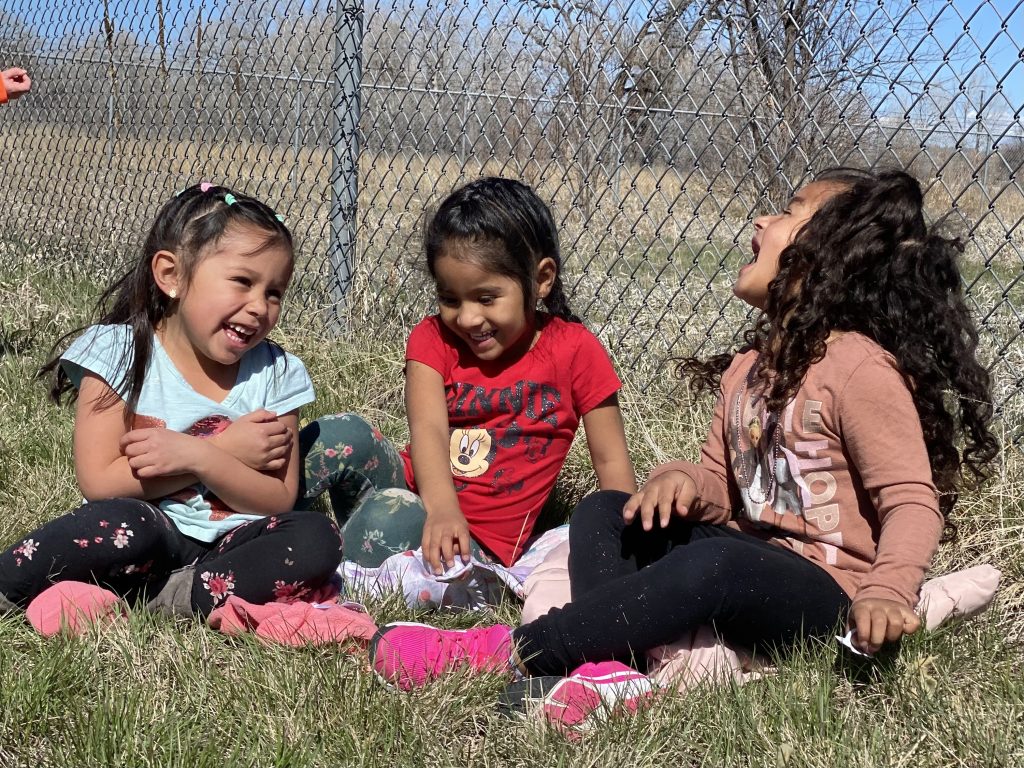 three young girls sitting in a field of grass laughing