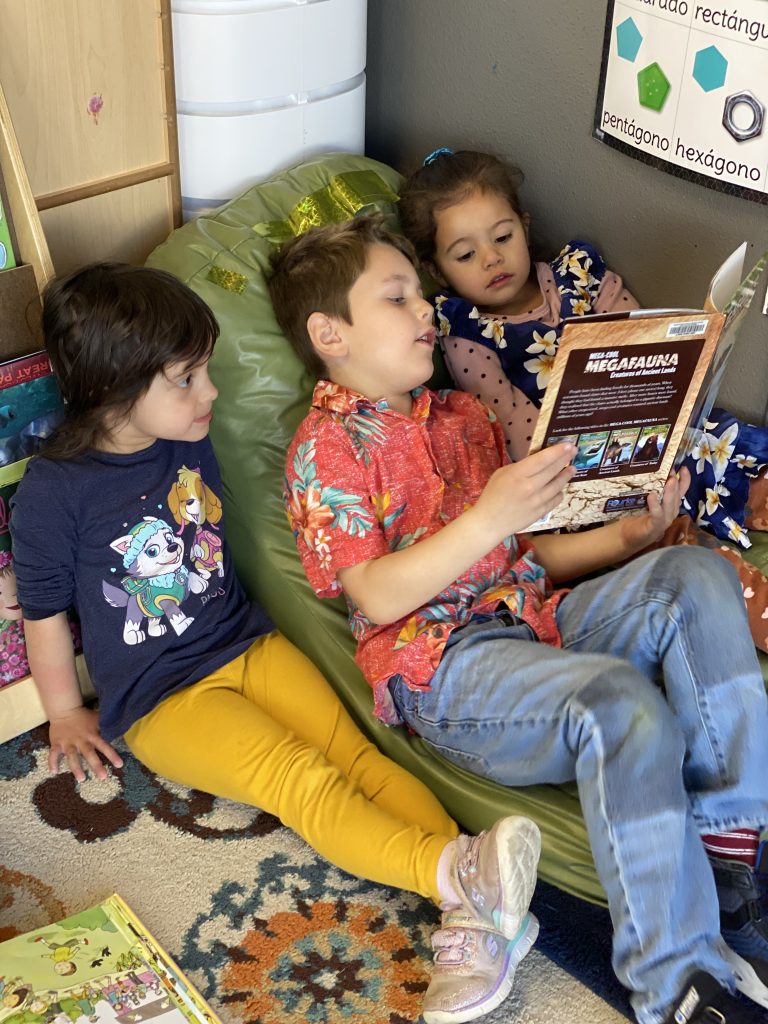 three children lay on a bean bag reading a book together