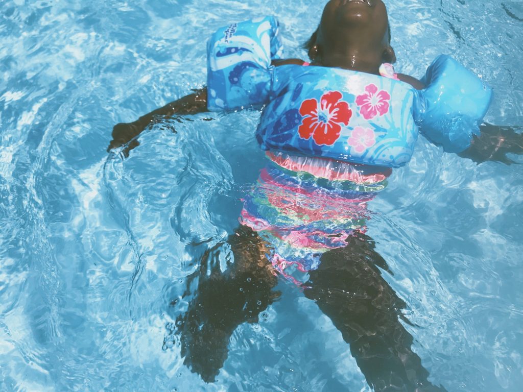 child floats on back in a pool with floaties on